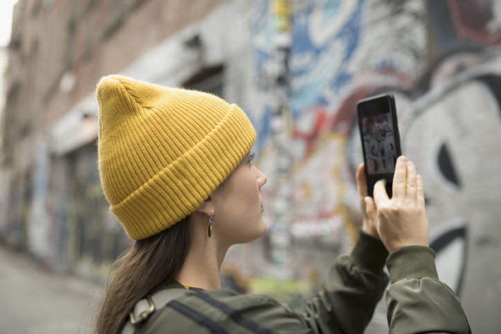 Young Woman With Camera Phone Photographing Graffiti On Urban Wall