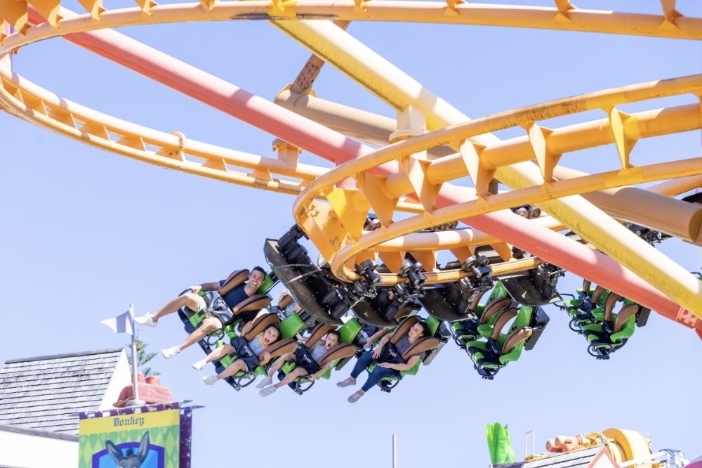 People ride a rollercoaster with smiles on their faces and their legs dangling in the air.