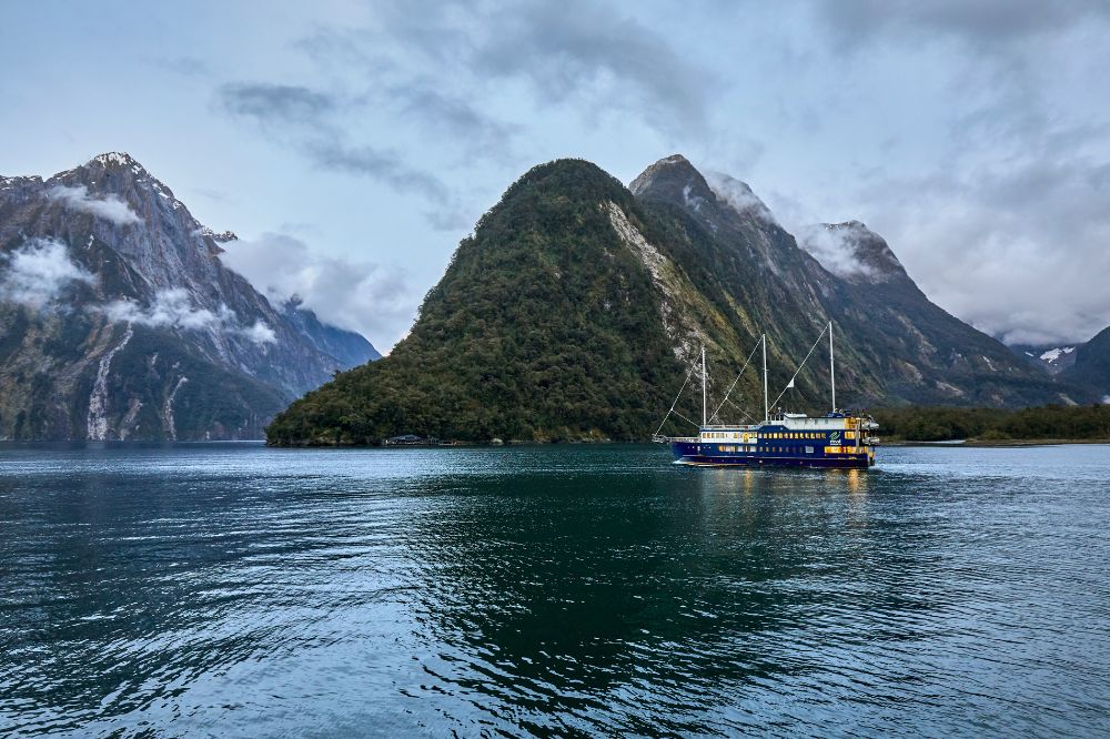A boat with three sails floats in the water surrounded by large rock formations covered in greenery.