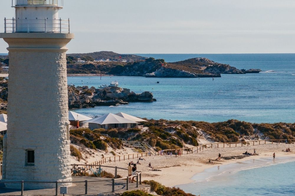 A lighthouse sits in the foreground. There are several beaches below with some people sitting or walking.