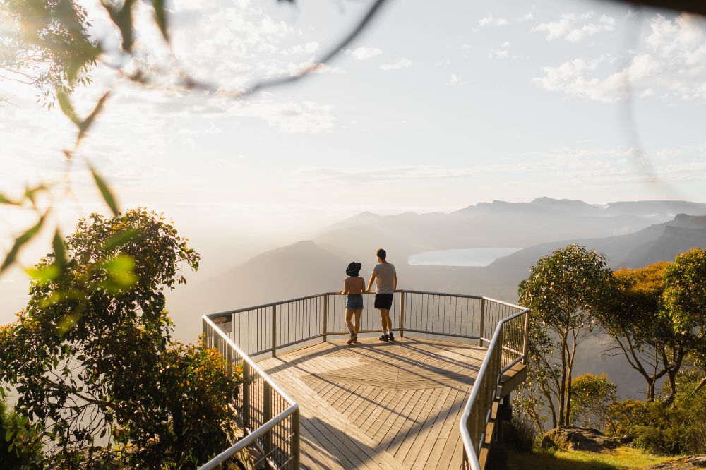 Two people stand on a lookout with vast mountains surrounding