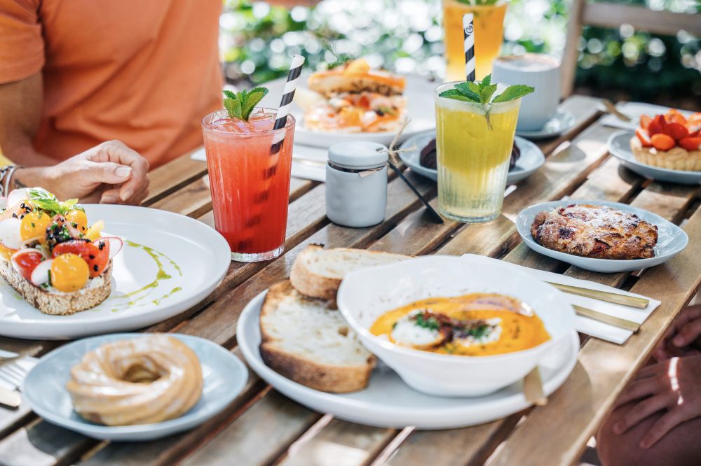 A table with plates of food and glasses of colourful drinks.