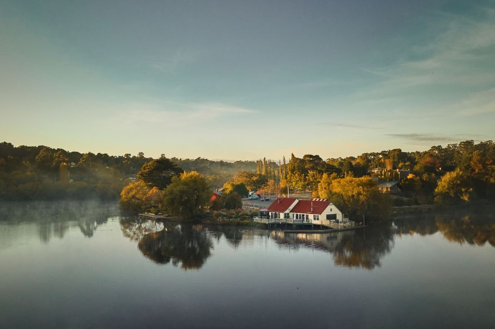 A still dark lake surrounded by trees with leaves turning orange in autumn