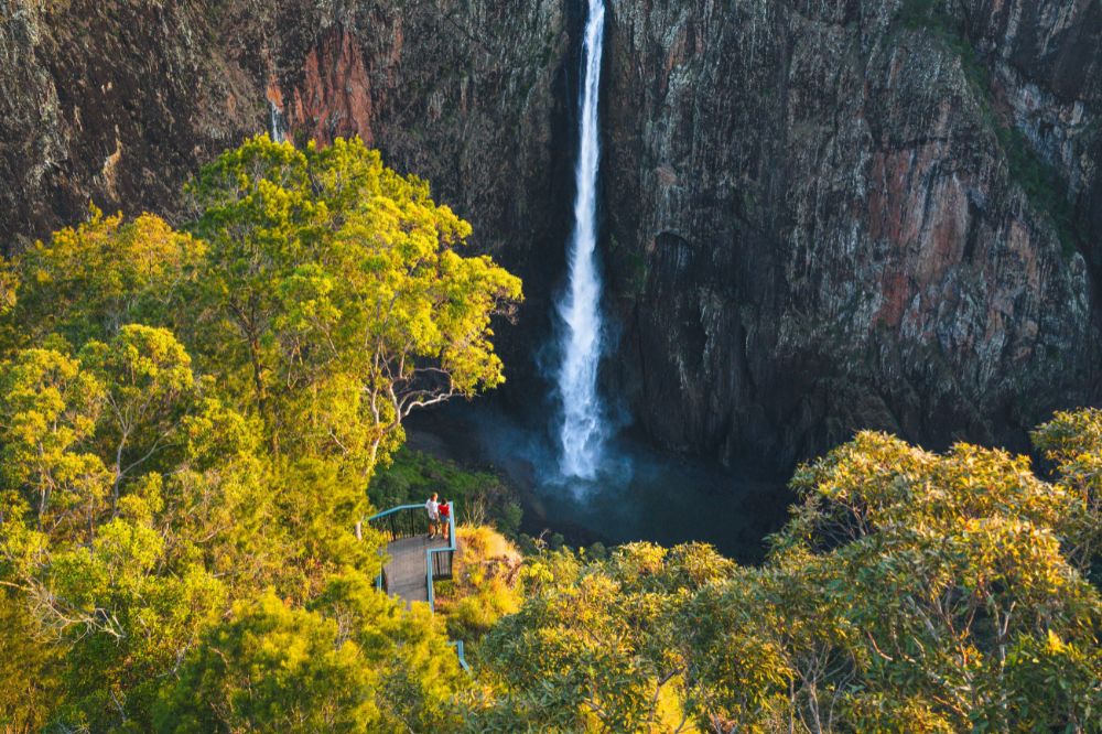 An aerial view of a couple surrounded by trees with yellow leaves looking out at a vast waterfall cascading down a steep rock face
