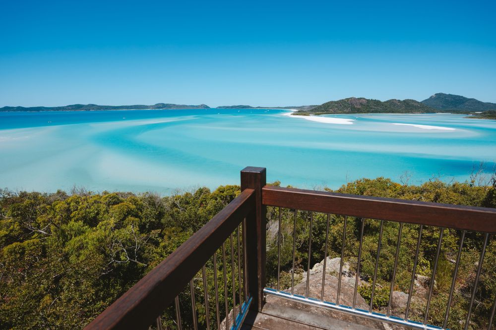 A viewpoint looking over a beach with bright blue water and white sand.