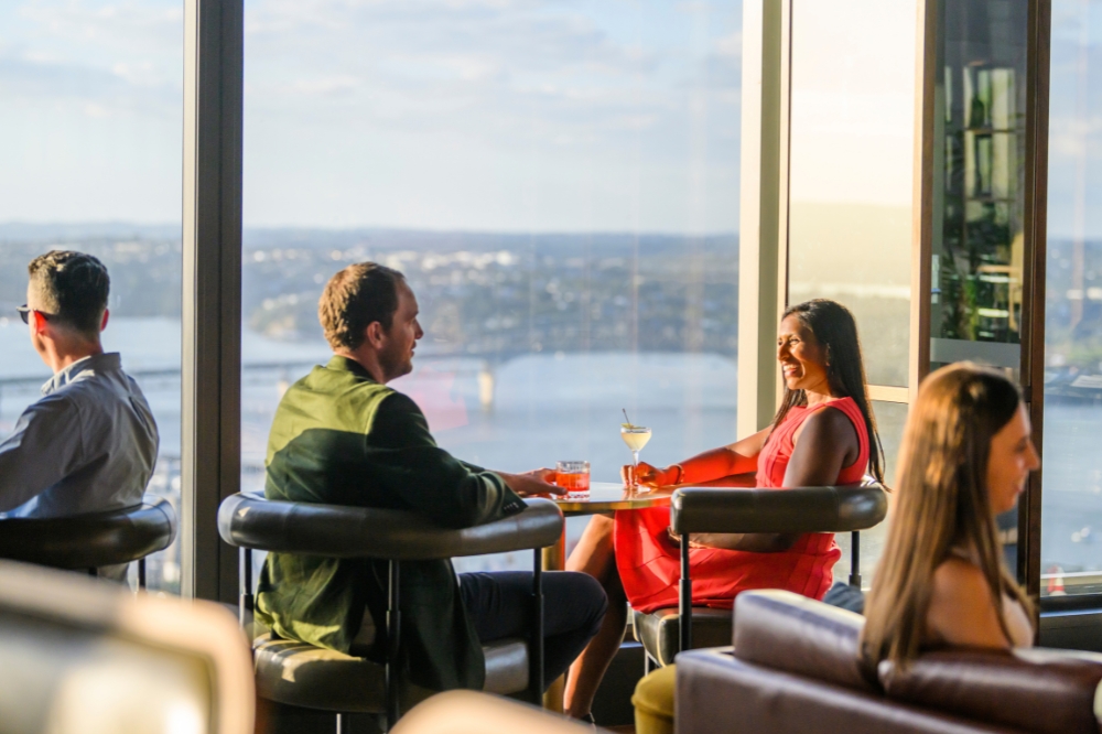 People sit with drinks in a high tower overlooking the water and Auckland city