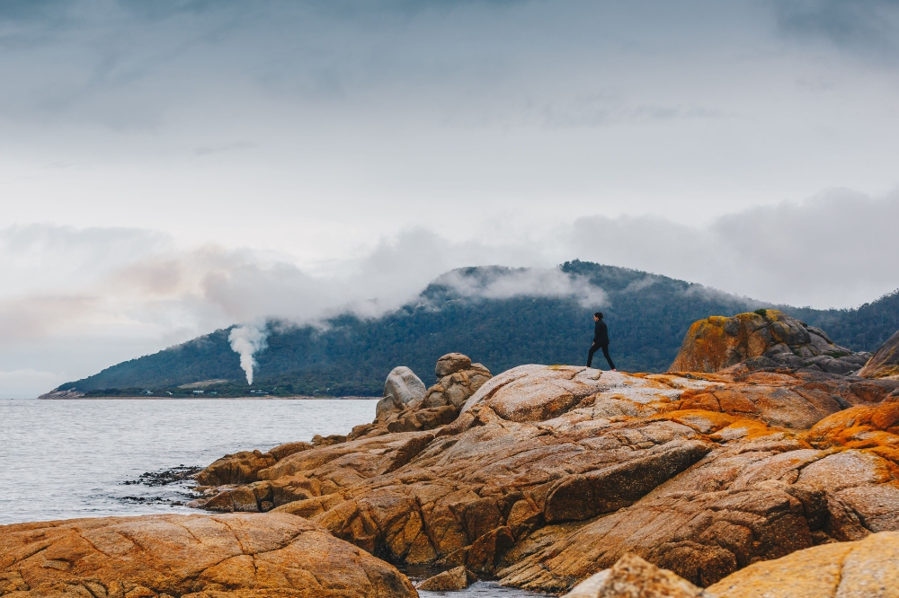 A person walks on red rocks on an overcast day with low clouds