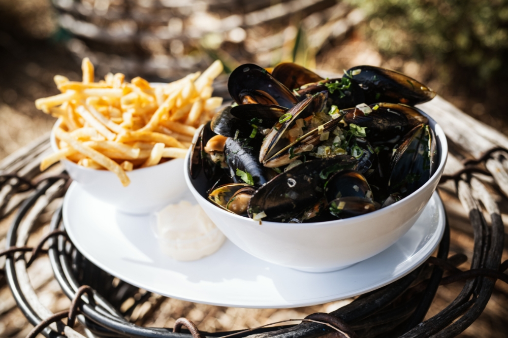 A large bowl of freshly cooked mussels and a bowl of fries sits on a table