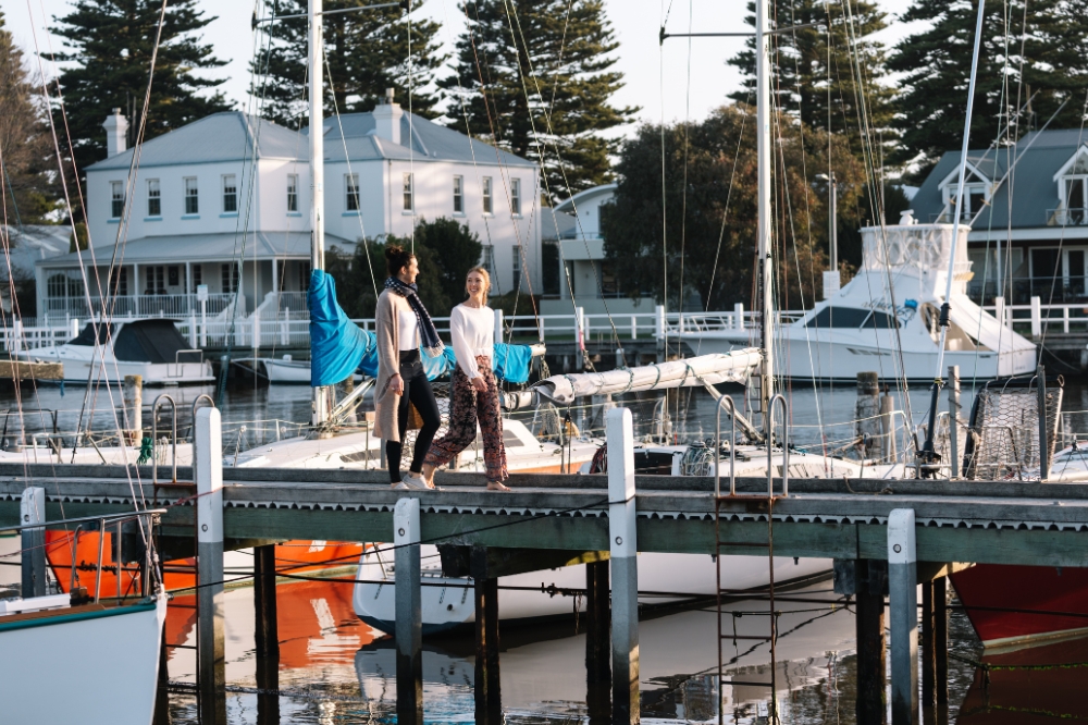 Two people walk along the waterfront, boats surround in the water