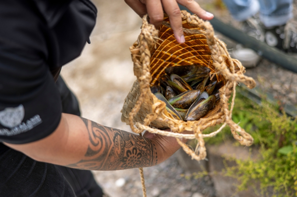 A person holds open a woven bag with fresh mussels