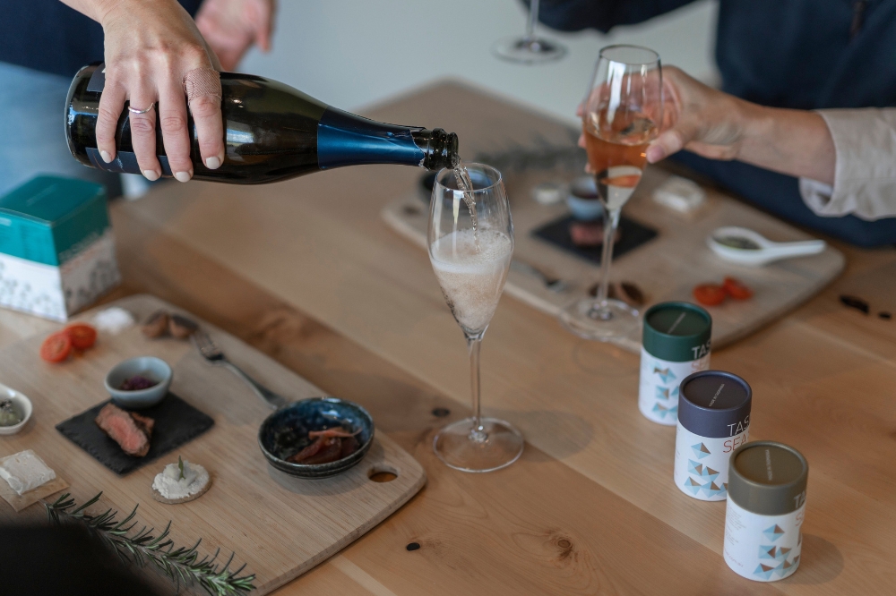 A person pours sparkling wine into a glass on a table with tasting boards neatly presented