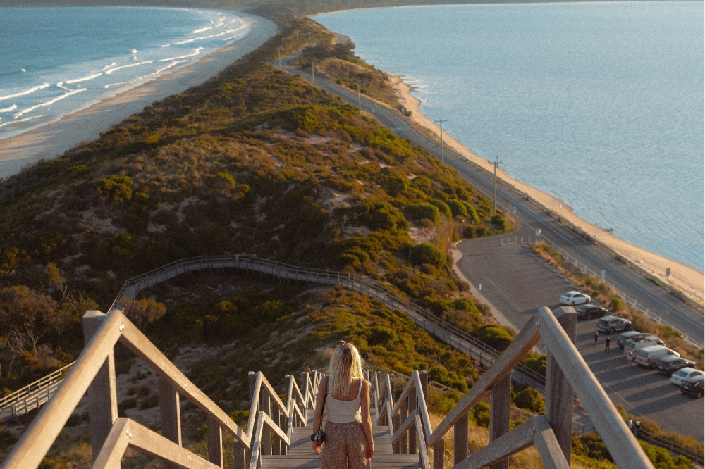 A person walks down a set of stairs leading to a boardwalk between two beaches