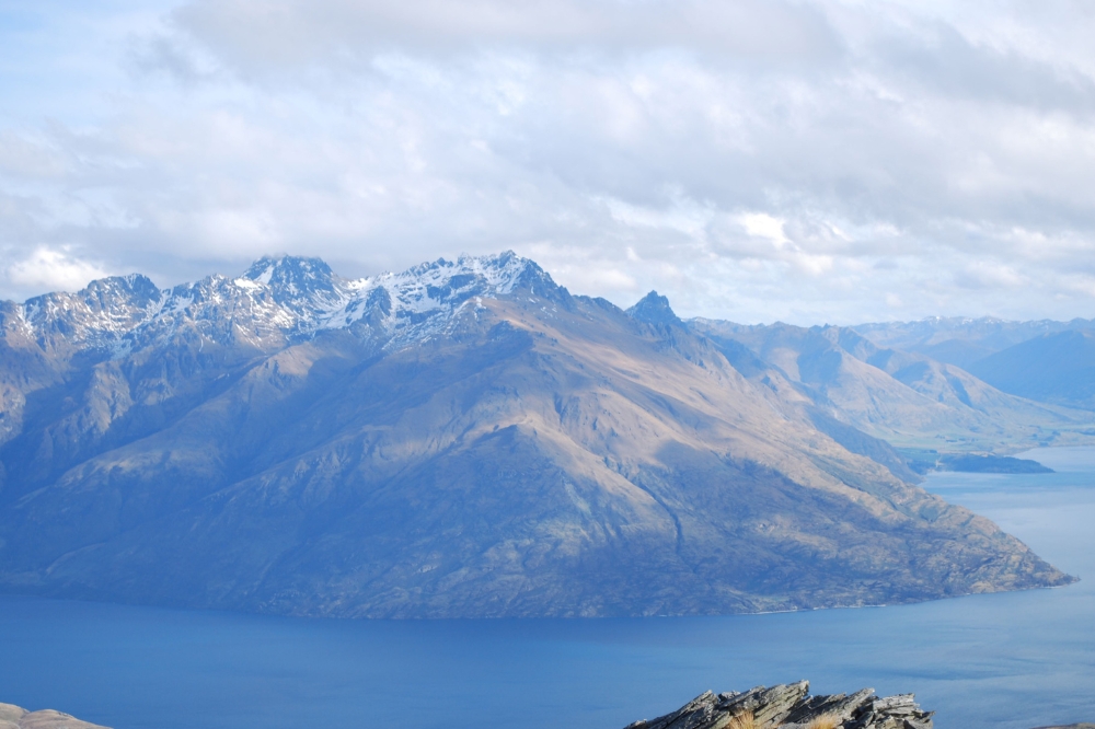 An aerial view of snow capped mountains surrounded by a still blue lake