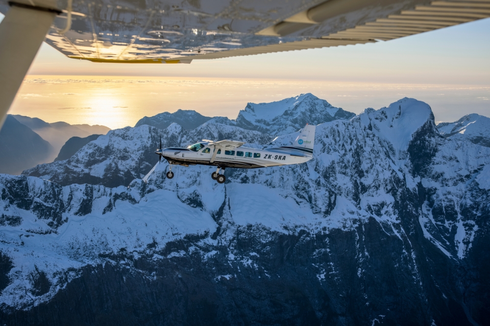 A small plane flies above snow capped mountain peaks