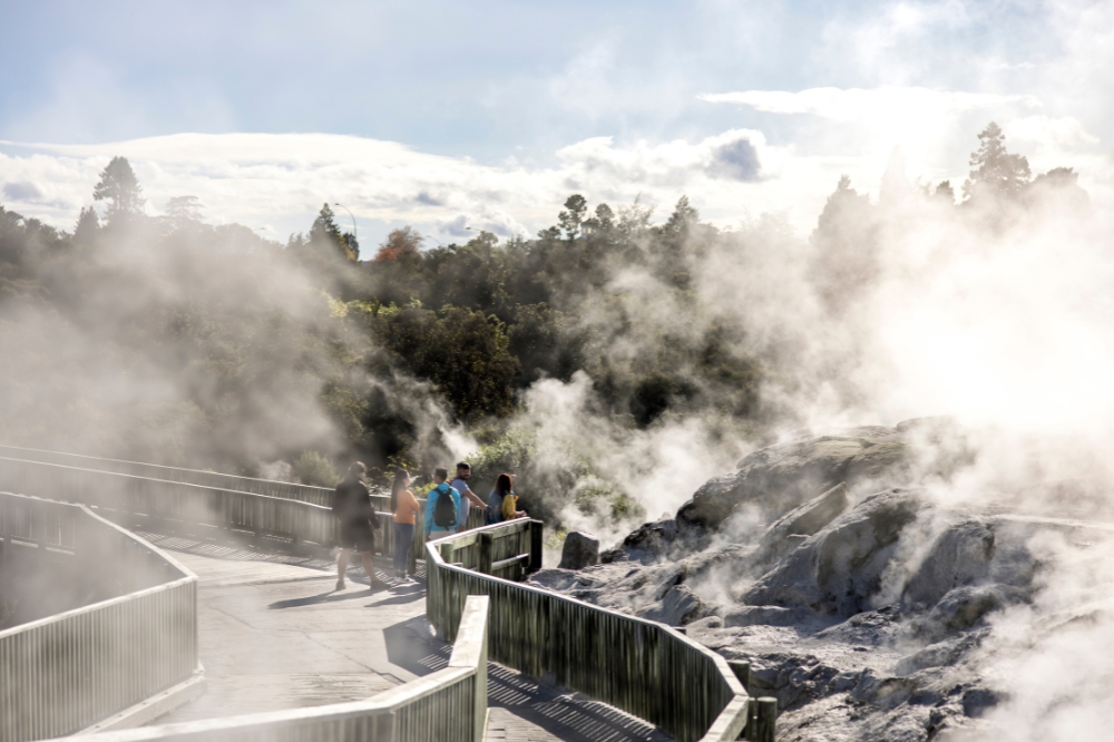 People walk along a boardwalk with steam rising from hot springs on either side