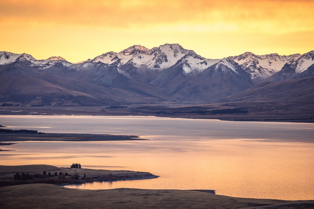 Snow capped mountains with a bright orange sky. The lake below reflects the orange light