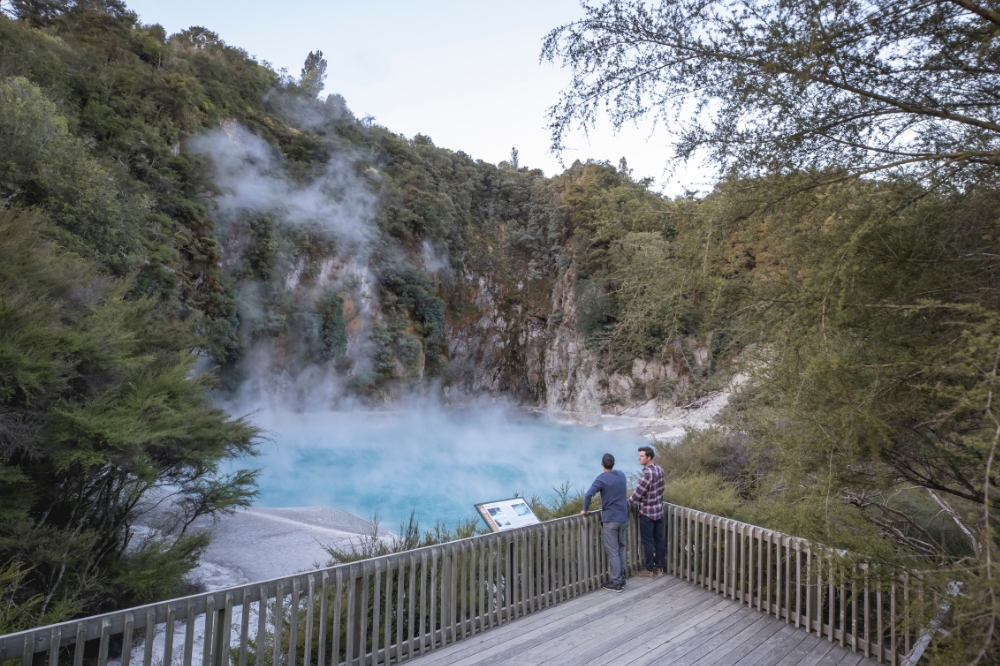 Two people stand on a boardwalk overlooking a hot spring
