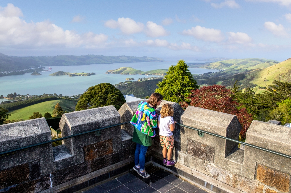 A family look over a castle wall with a lake in the background